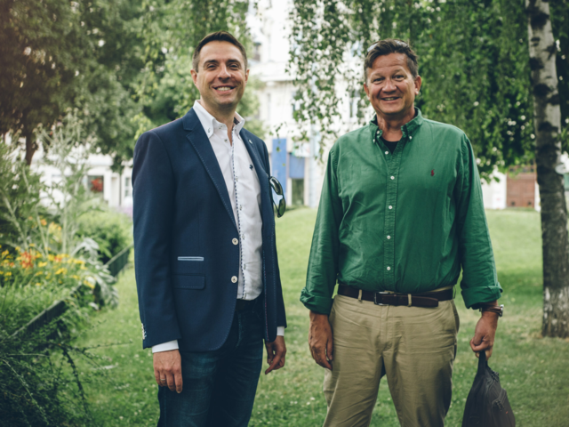 Estate agent Christian Koch and Christian Hilscher stand in a park and are happy about their successful collaboration in property marketing